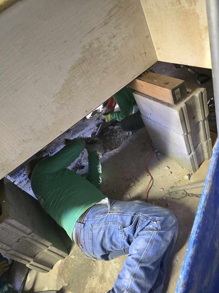 Person in green shirt and jeans working under a structure, possibly construction or repair.