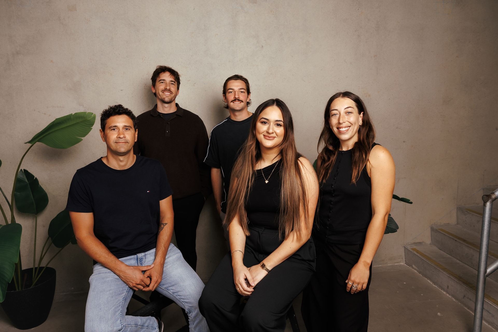 A diverse group of professional colleagues stand together in a bright, modern office, smiling toward the camera.