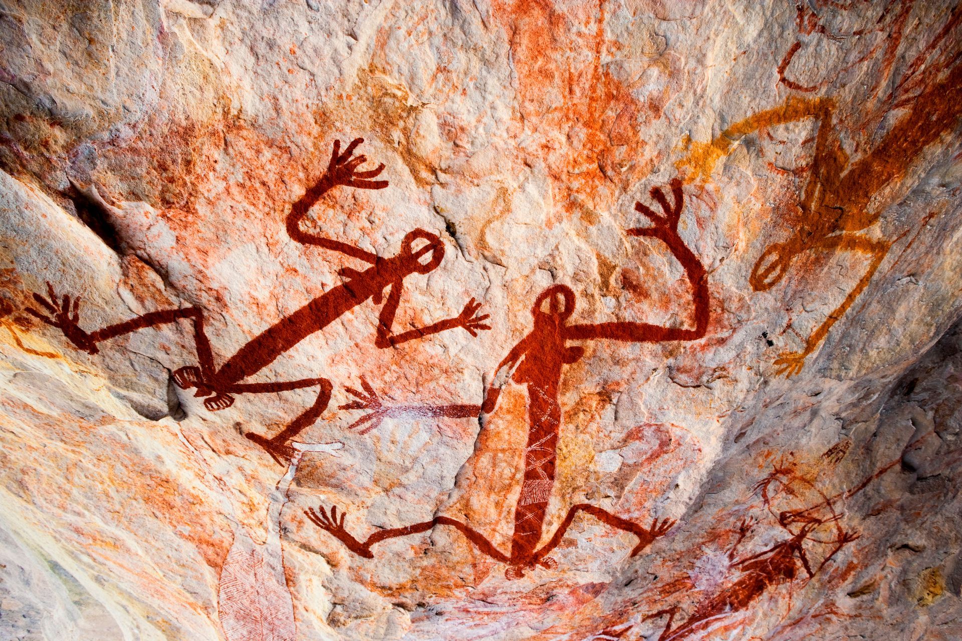 Ancient rock art featuring red-pigmented figures with outstretched limbs painted on a textured stone surface.