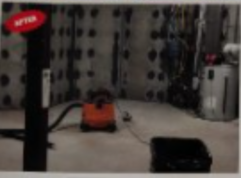 Orange vacuum cleaner in a basement, next to a black box. 