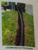 A black drainage pipe installed in a trench on a grassy lawn.