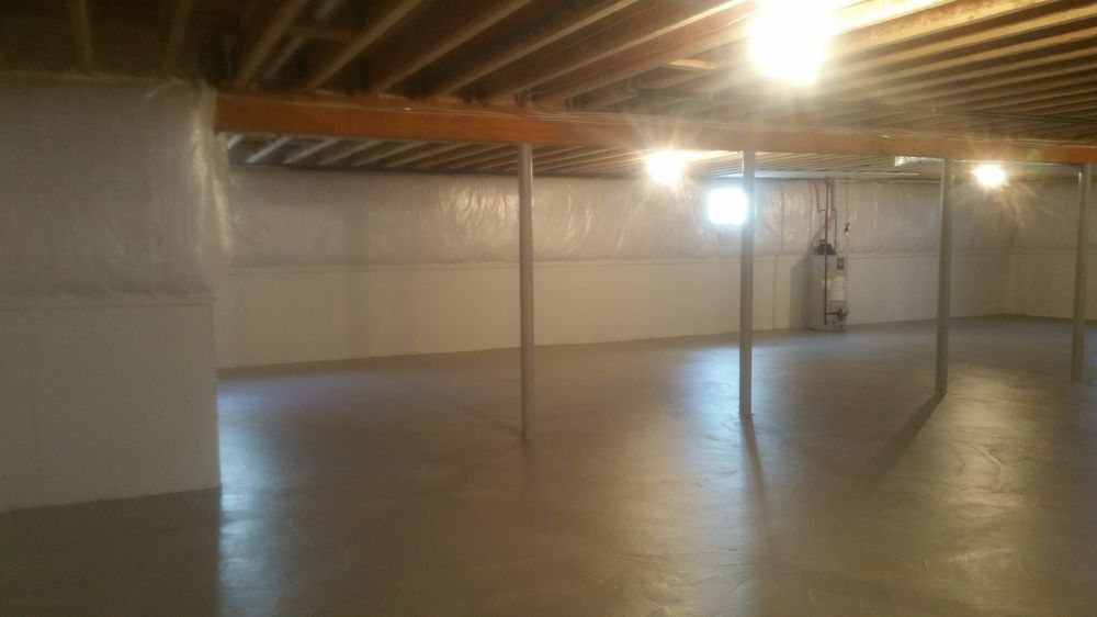 A finished basement with a concrete floor, support beams, and overhead lighting.