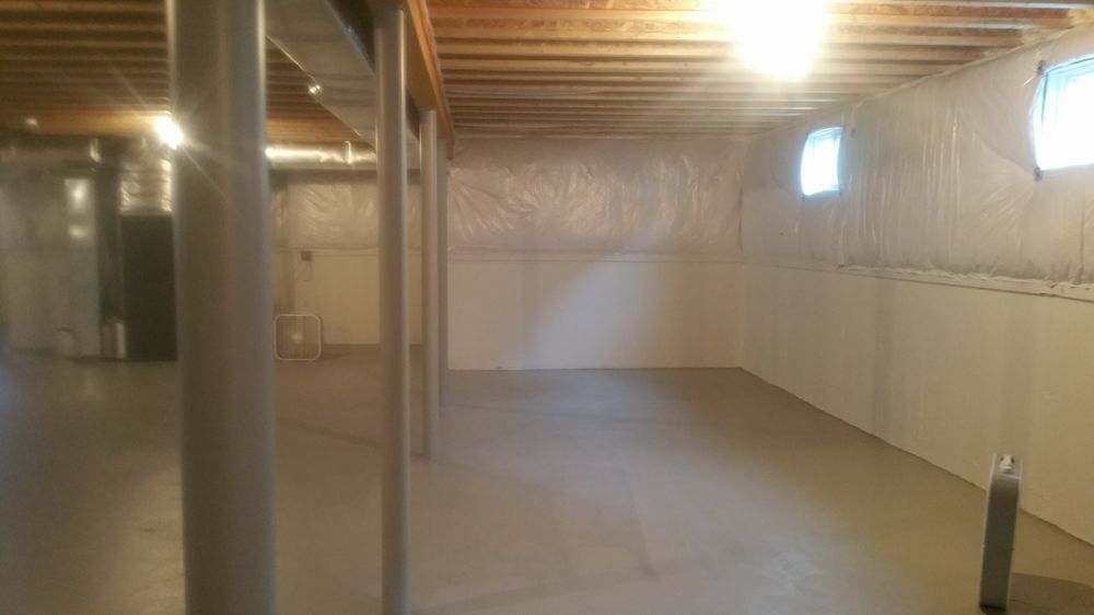 Empty unfinished basement with concrete floor, support beams, and white walls.
