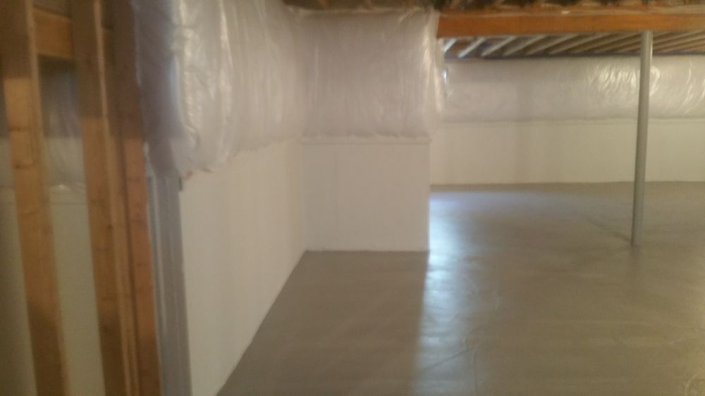 Finished basement with gray concrete floor, white walls, and exposed wooden beams.