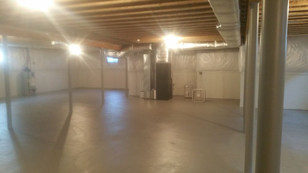 Empty basement with exposed beams, concrete floor, and insulation; pipes and a furnace are visible.