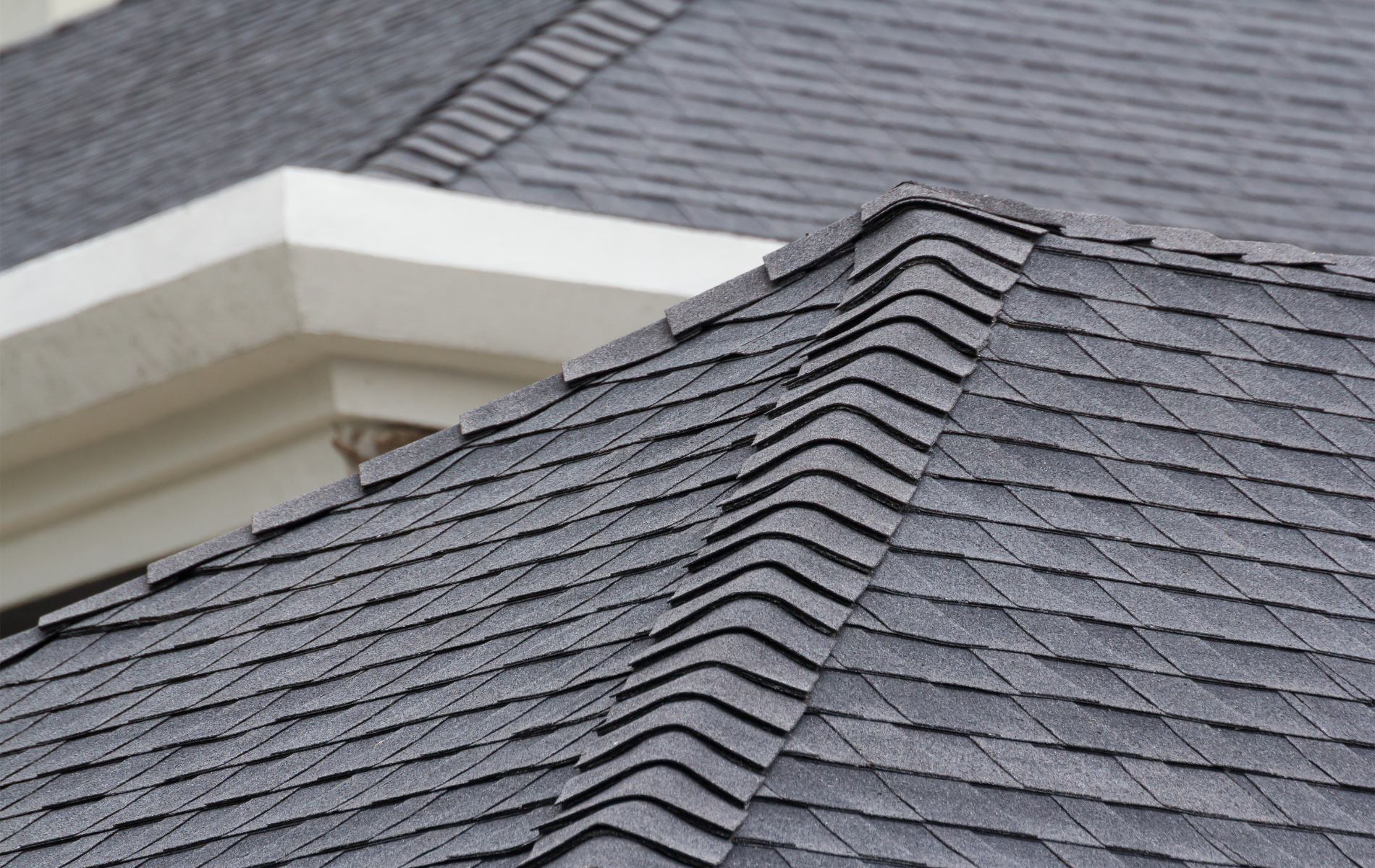Close-up of a gray asphalt shingle roof with a raised ridge and white trim.