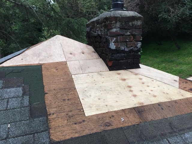 Roofer wearing a hard hat and gloves repairs a damaged tile roof with a hammer.
