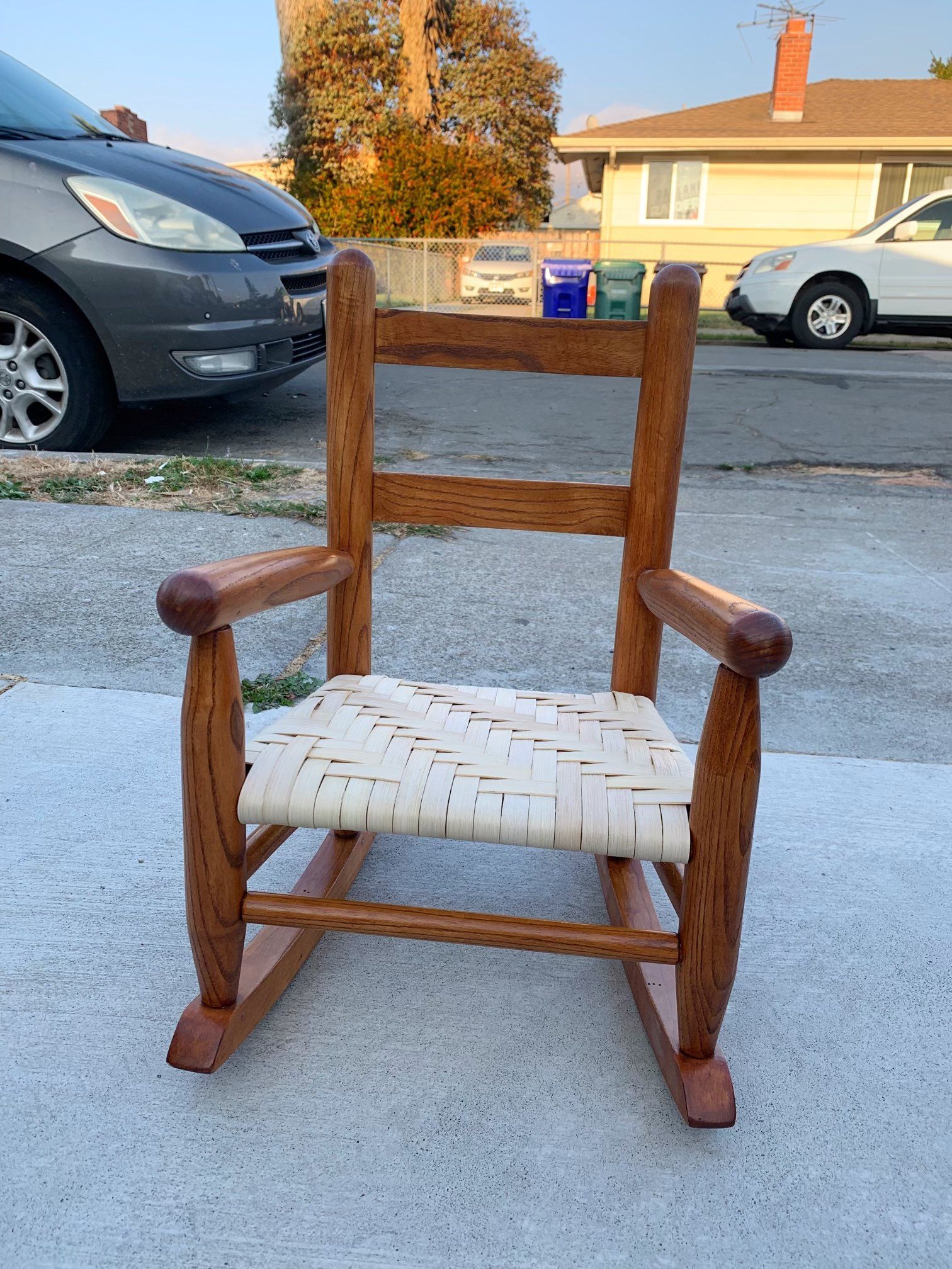 A wooden rocking chair with a white seat is parked on the side of the road