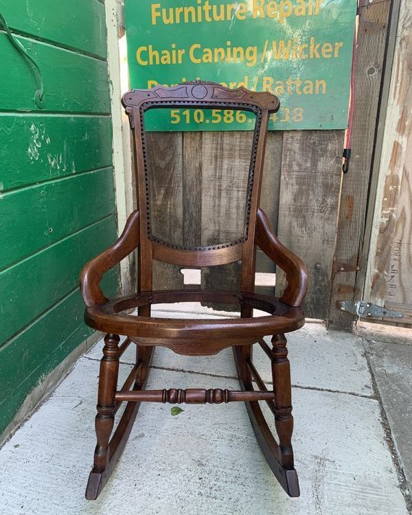 A wooden rocking chair is sitting in front of a sign that says furniture repair