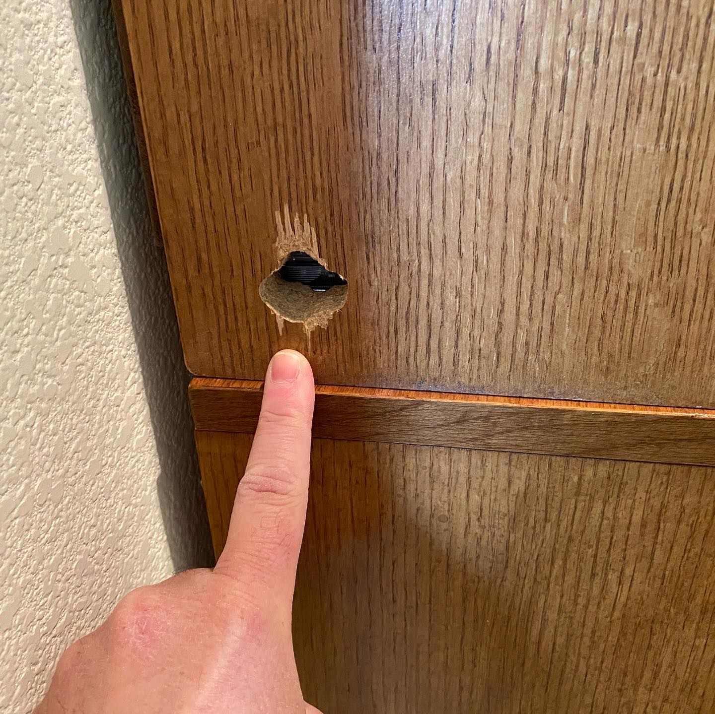 A person is pointing at a hole in a wooden door.