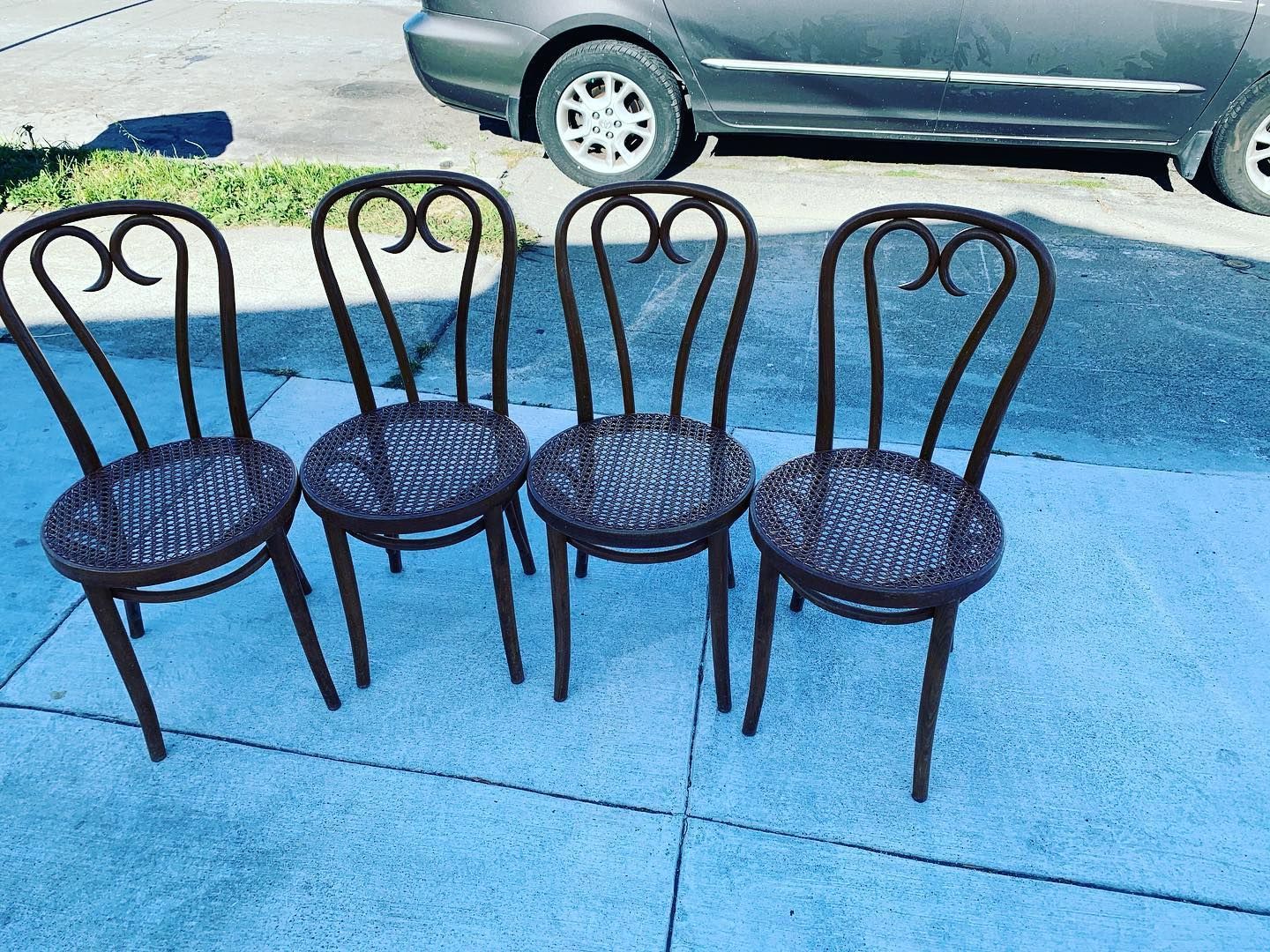 Four chairs are lined up on a sidewalk in front of a car