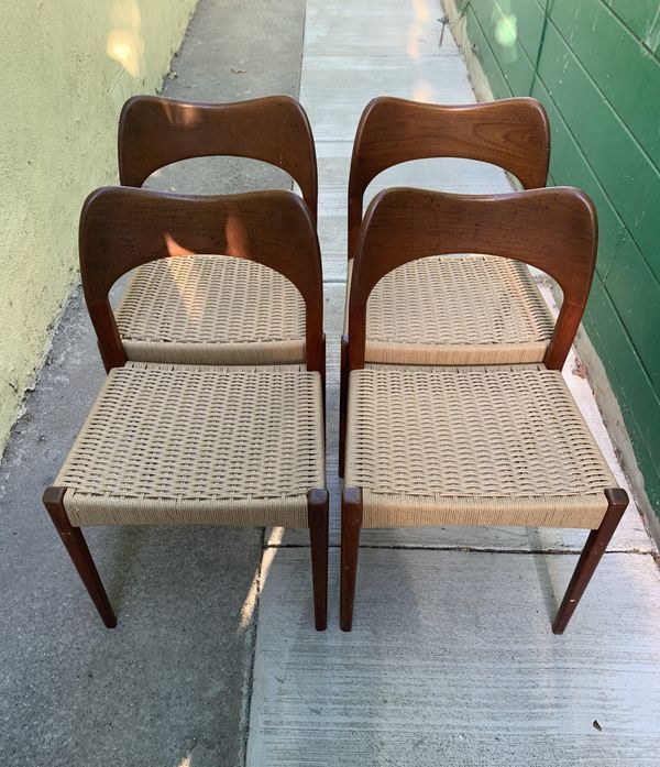Four wooden chairs with wicker seats are sitting on a sidewalk