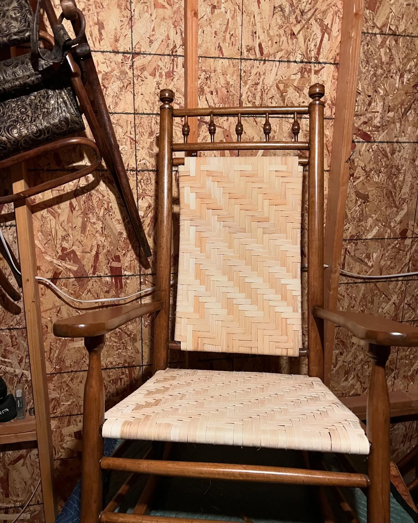 A wooden rocking chair with a wicker seat is sitting in a room.