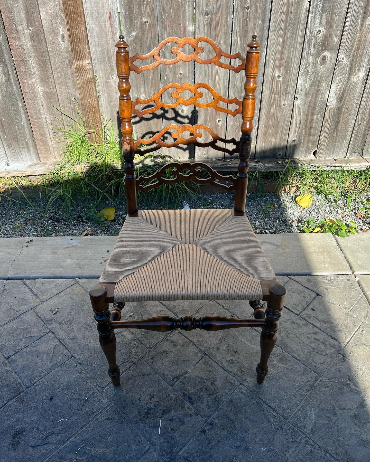 A wooden chair with a wicker seat is sitting in front of a wooden fence.