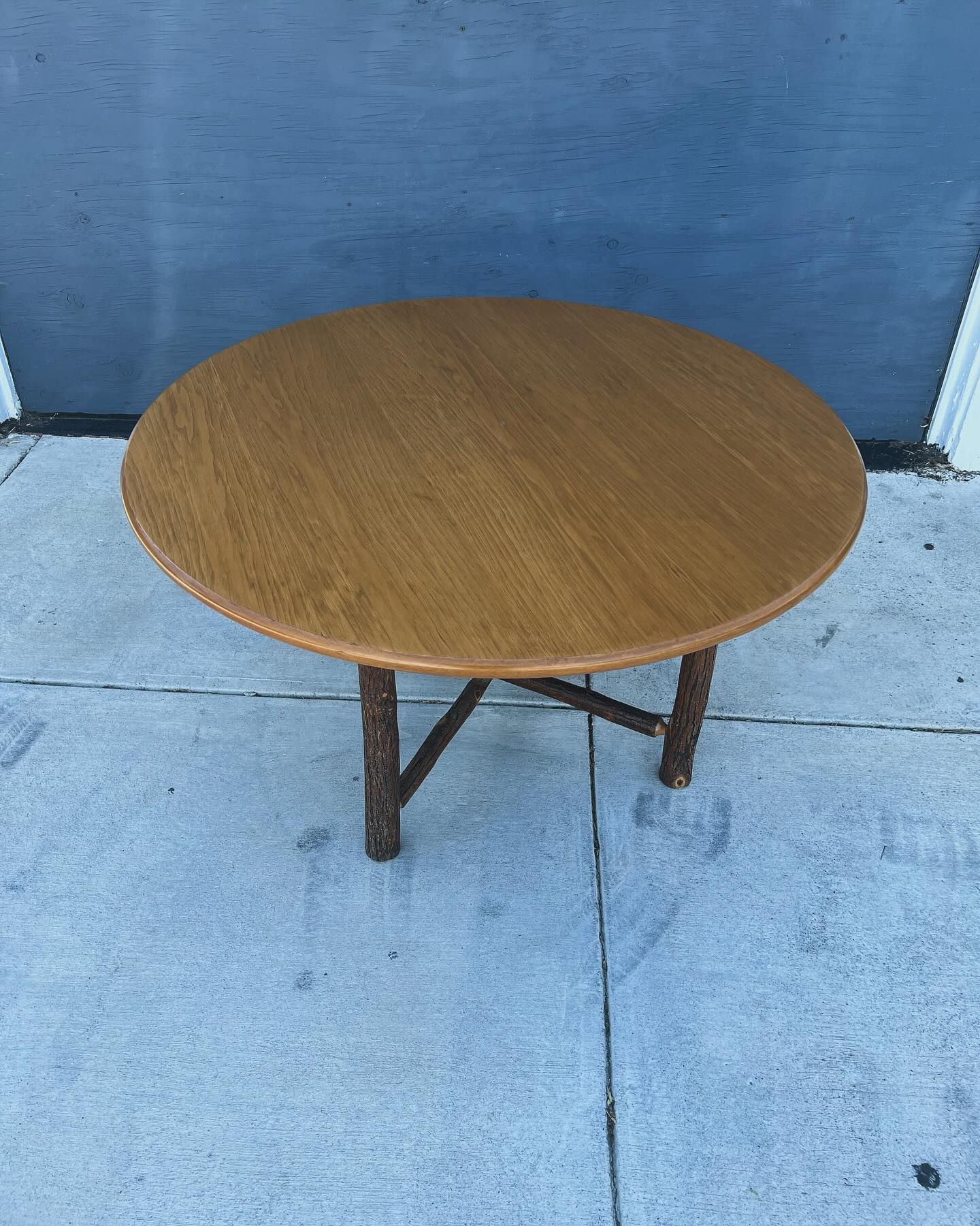 A round wooden table is sitting on a sidewalk in front of a blue door.