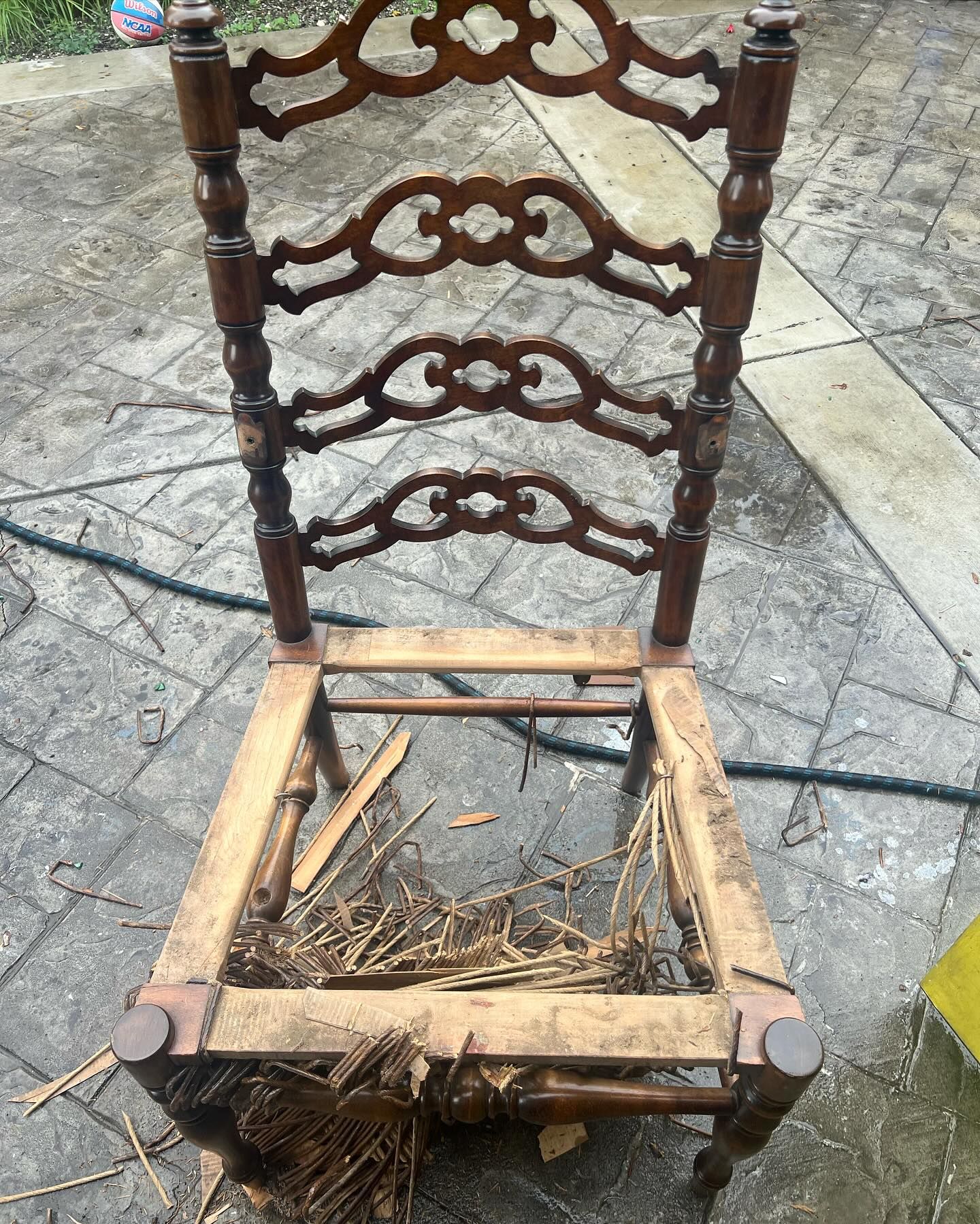 A wooden chair with a broken seat is sitting on a brick sidewalk.