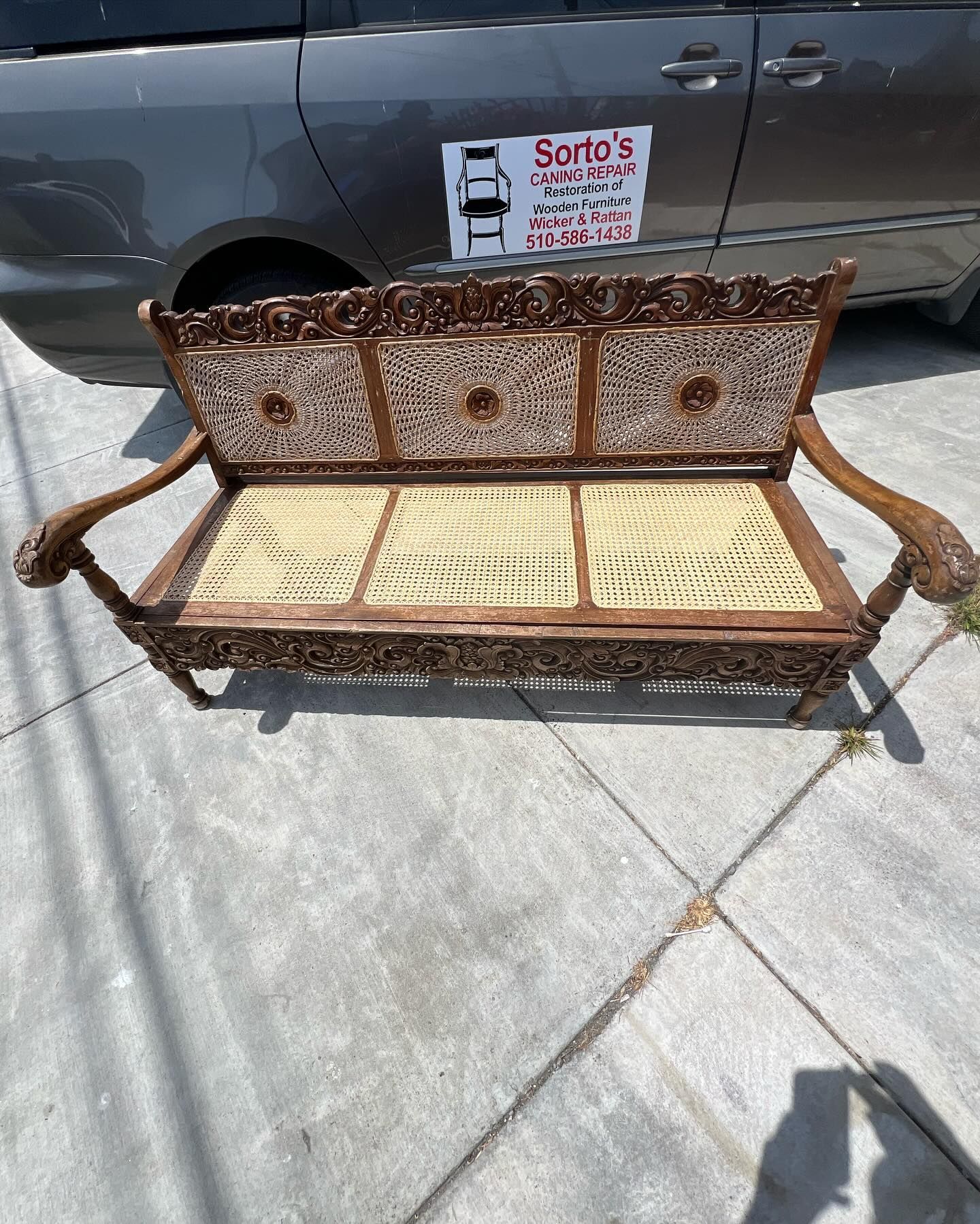A wooden bench is sitting on a sidewalk next to a car.