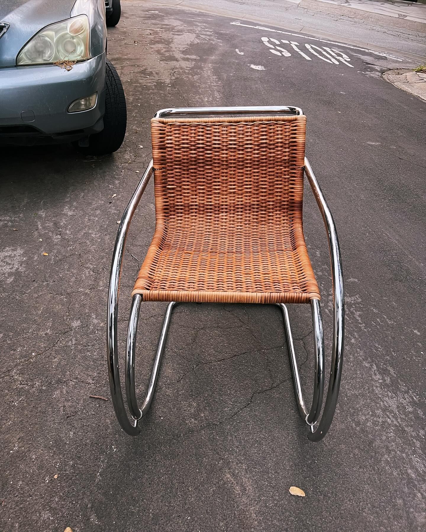 A wicker chair is sitting on the side of the road next to a car.