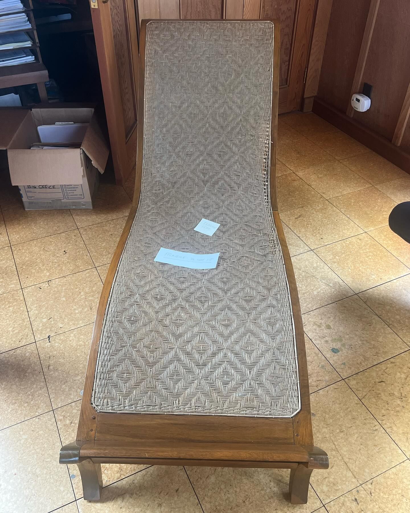 A wooden lounge chair is sitting on a tiled floor in a room.