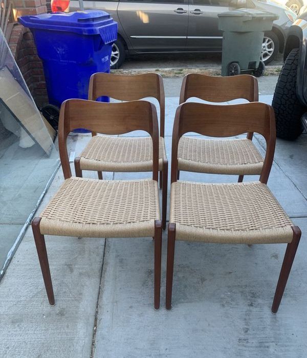 Four wooden chairs with wicker seats are lined up on a sidewalk