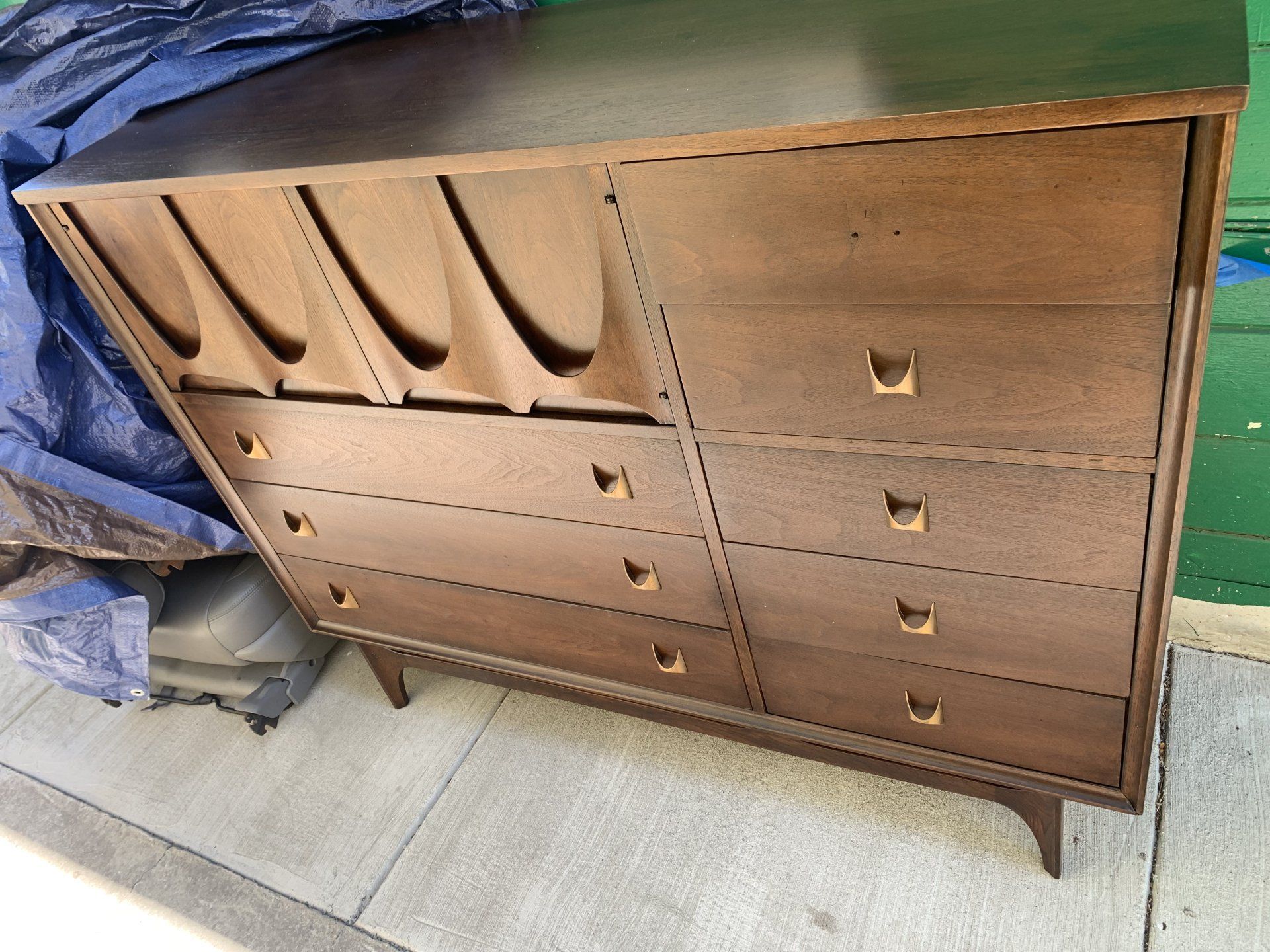 A wooden dresser is sitting on a sidewalk next to a blue tarp.