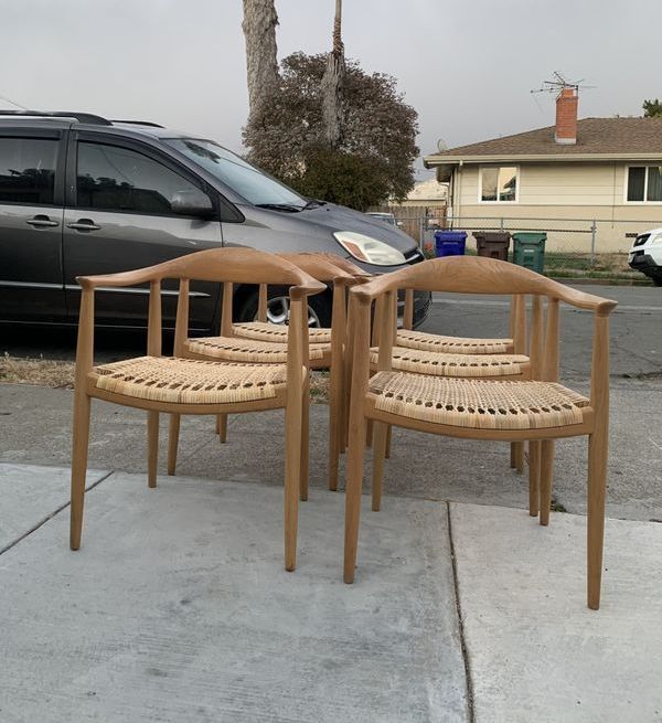 Four wooden chairs are sitting on a sidewalk in front of a car