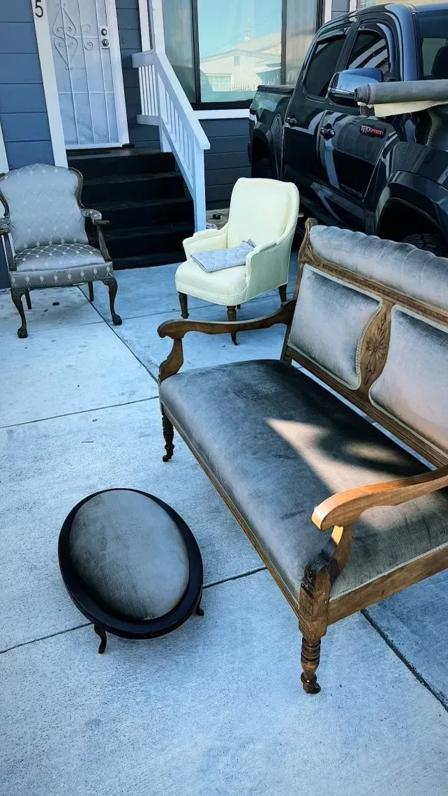A row of chairs and a couch are sitting on a sidewalk in front of a house.