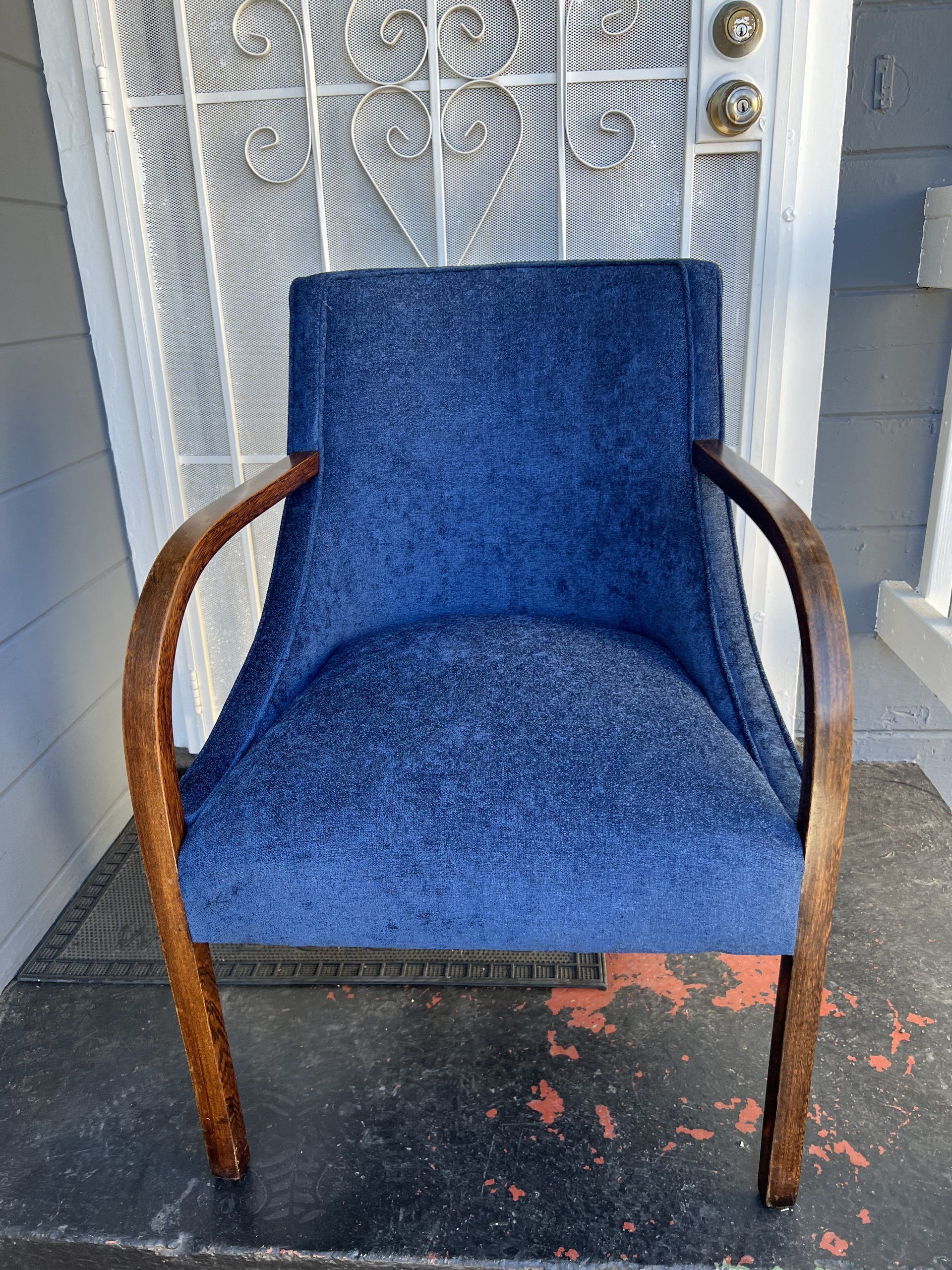 A blue chair is sitting on a porch in front of a door.
