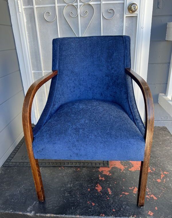 A blue chair with wooden arm rests is sitting in front of a door.