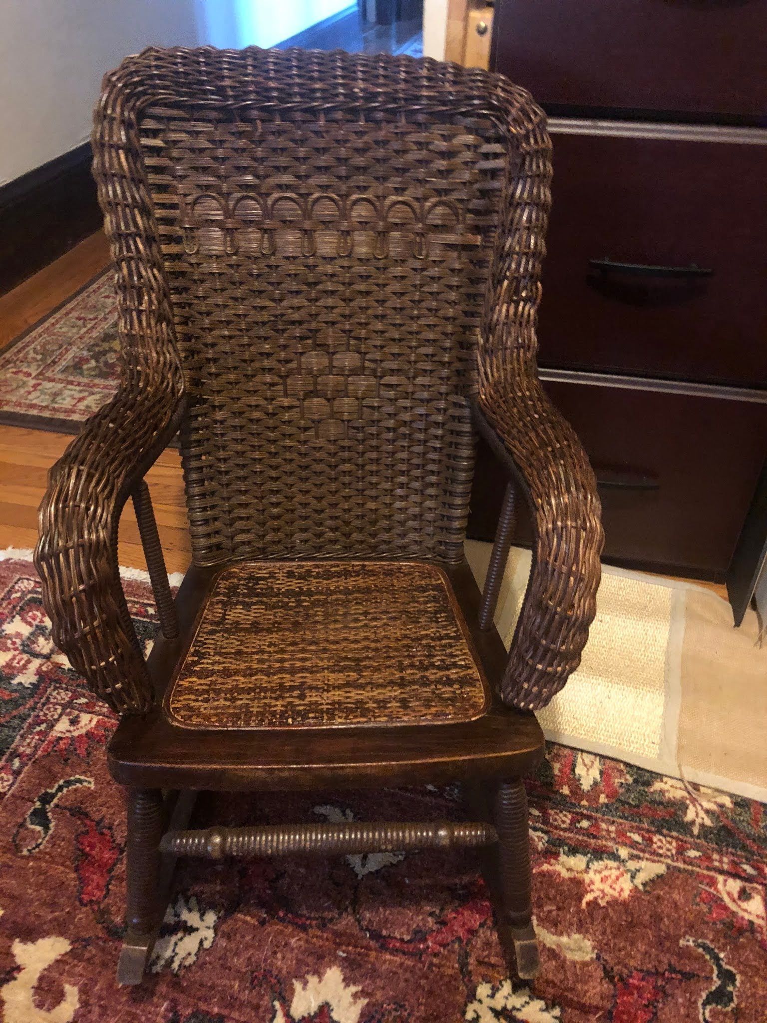 A wicker rocking chair is sitting on a rug in a room.