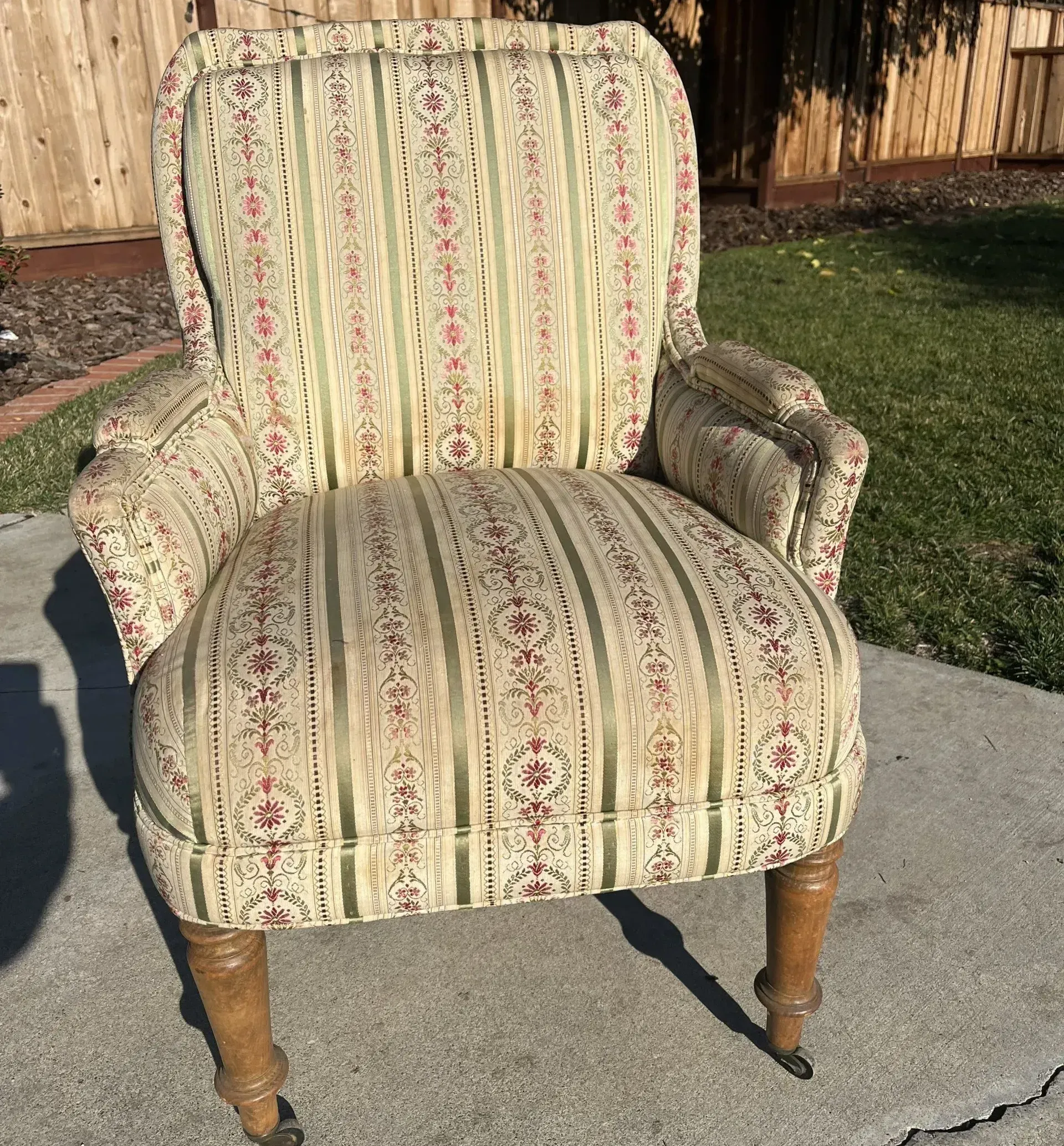 A chair with a striped fabric and wooden legs is sitting on a sidewalk.
