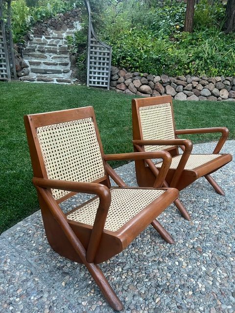 Two wooden chairs with wicker seats are sitting on a gravel patio
