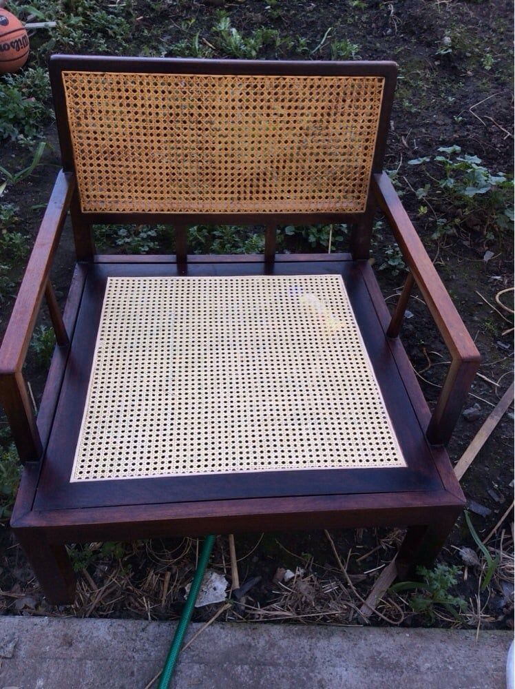 A chair with a wicker seat is sitting on a sidewalk next to a hose.