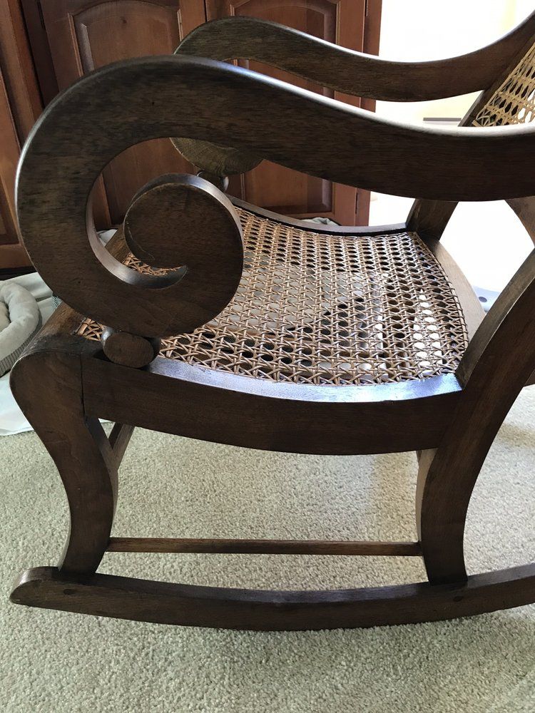A wooden rocking chair with a wicker seat is sitting on a carpeted floor.