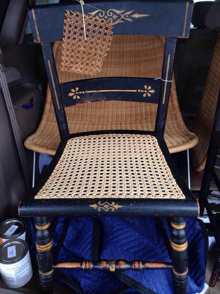 A black chair with a wicker seat is sitting in the back of a car.