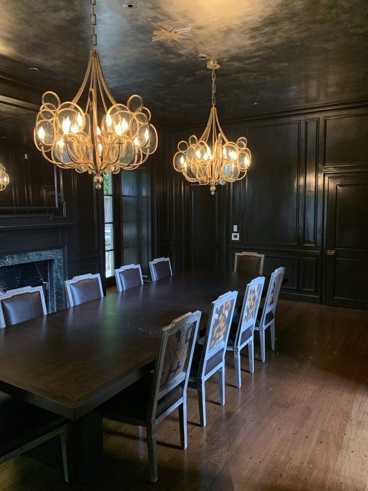 A dining room with a long table and chairs and two chandeliers hanging from the ceiling.