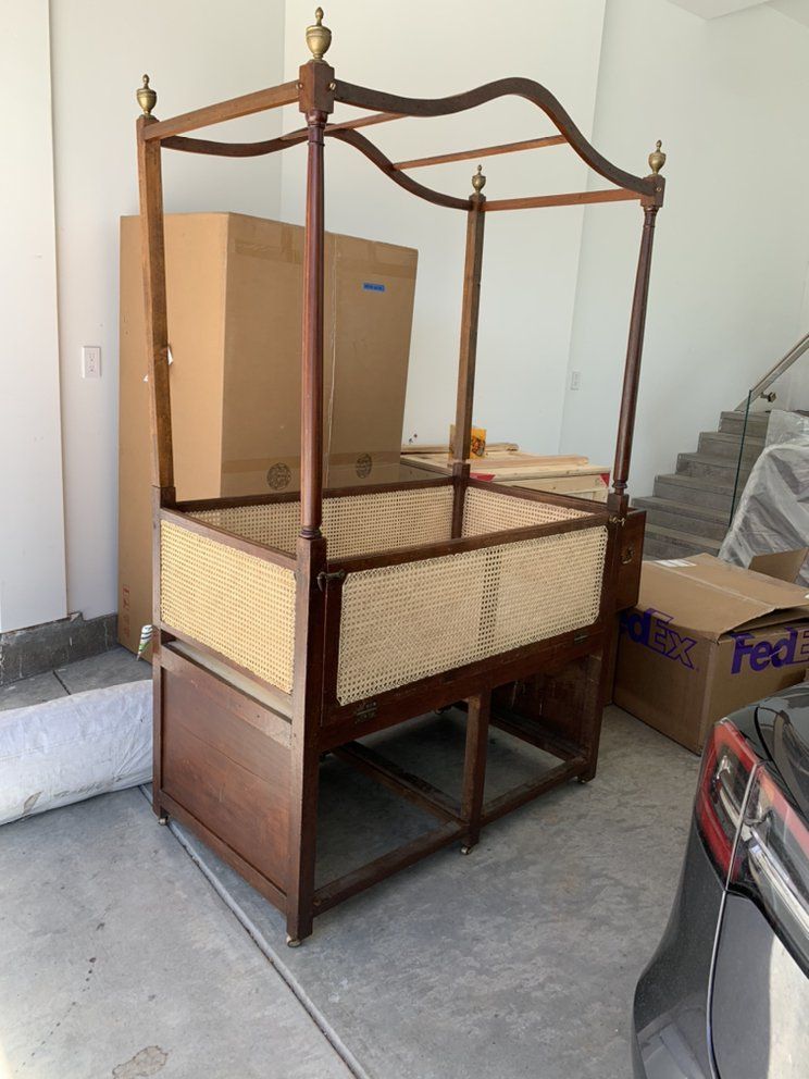 A canopy bed is sitting in a garage next to a fedex box.