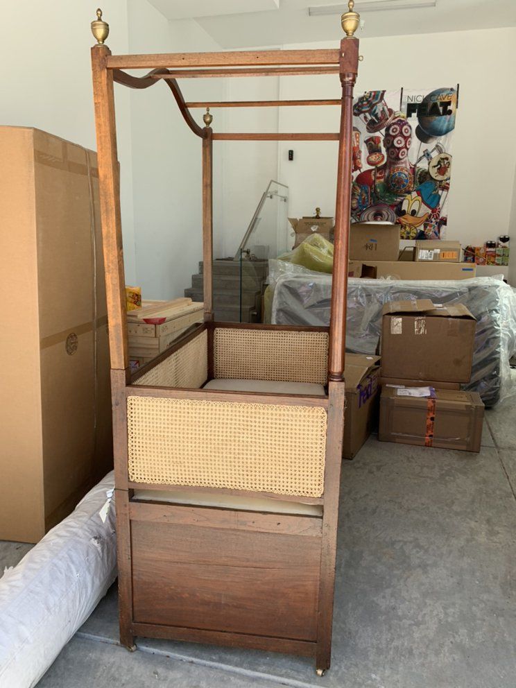 A canopy bed is sitting in a garage surrounded by boxes.