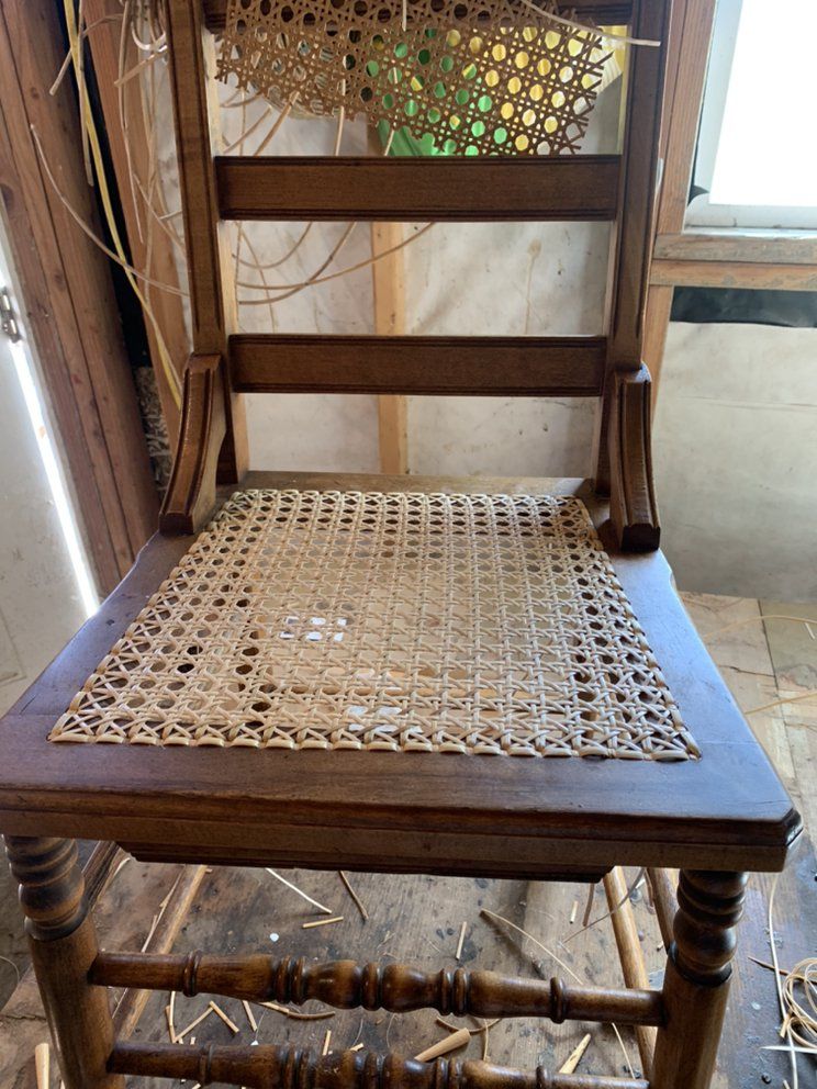 A wooden chair with a wicker seat is sitting on a wooden floor.
