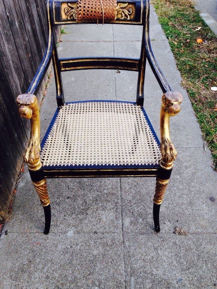 A black and gold chair with a wicker seat sits on a sidewalk