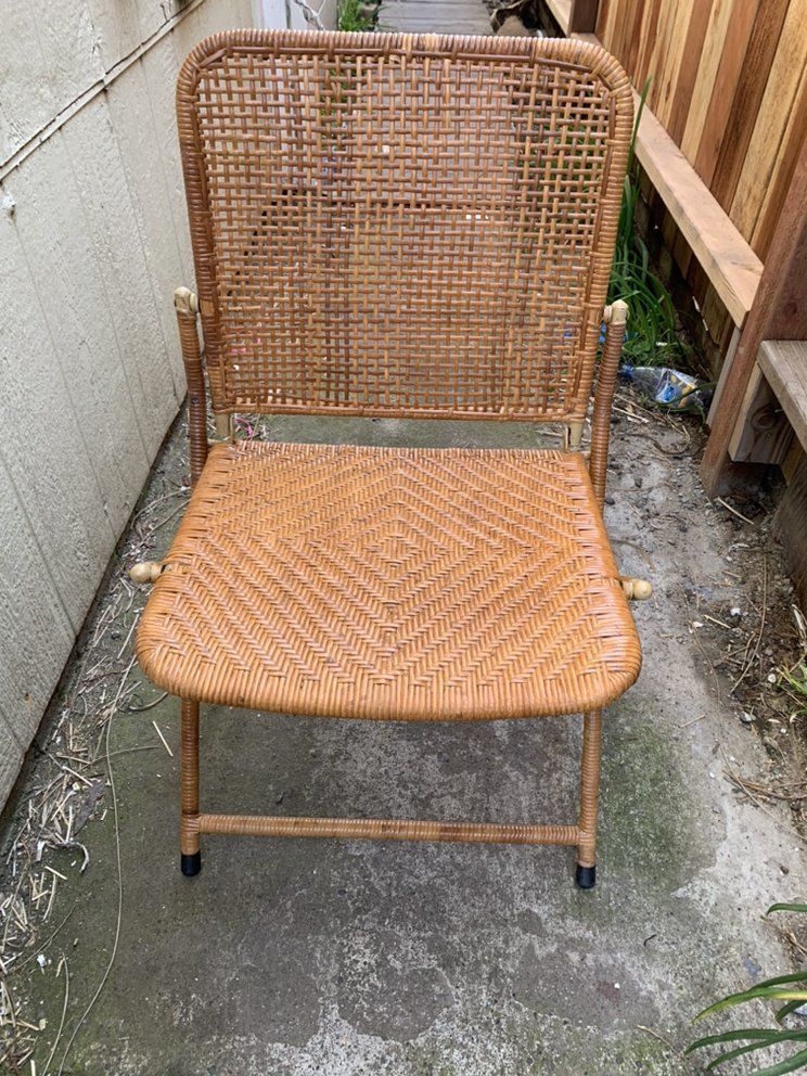 A wicker chair is sitting on a sidewalk next to a fence.