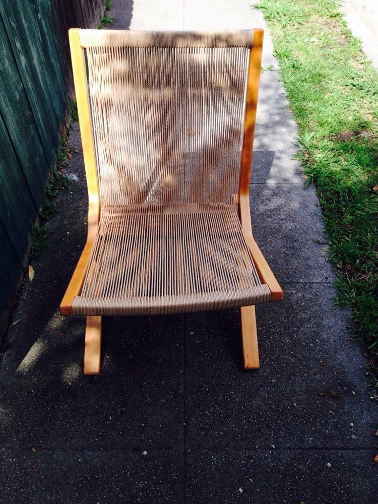 A wooden chair is sitting on a sidewalk next to a grassy area.