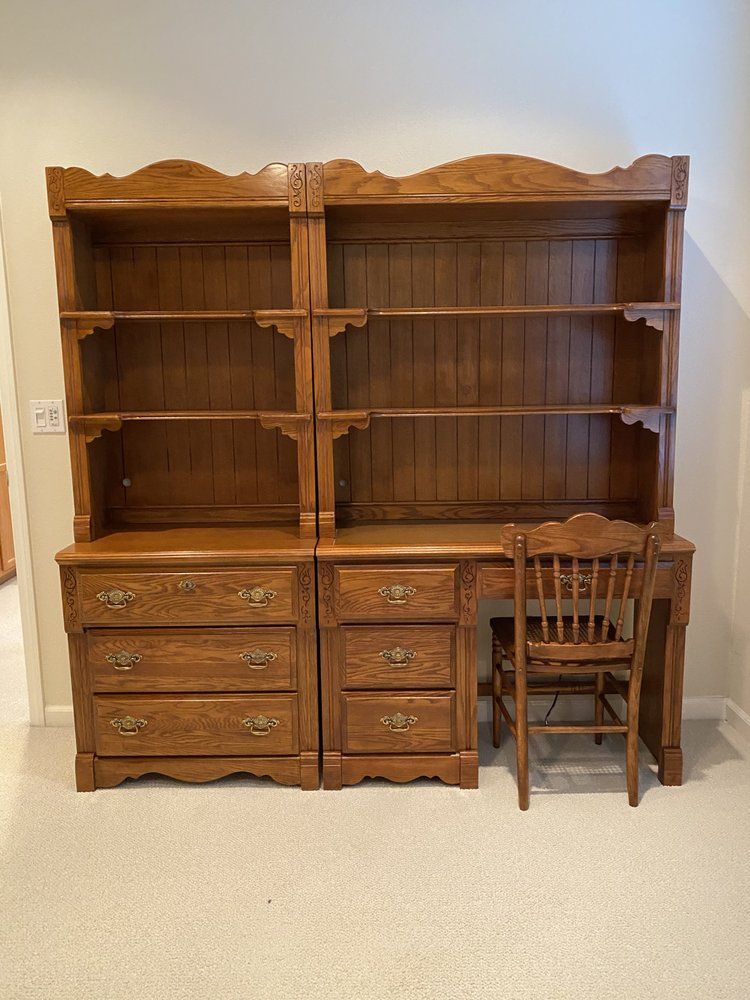 A wooden desk with a chair and shelves in a room.