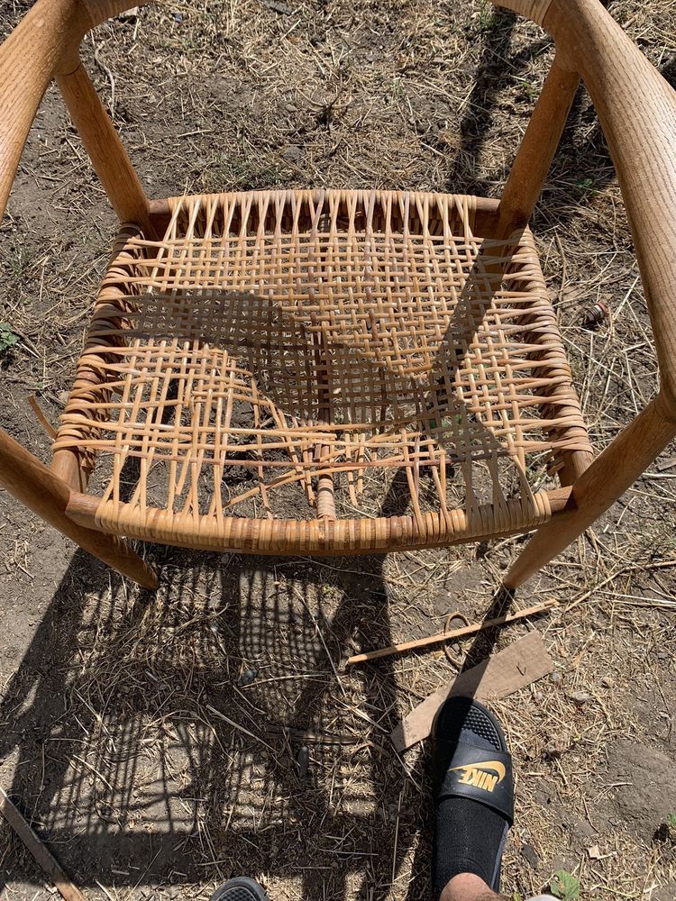A person is standing next to a wicker chair on the ground.