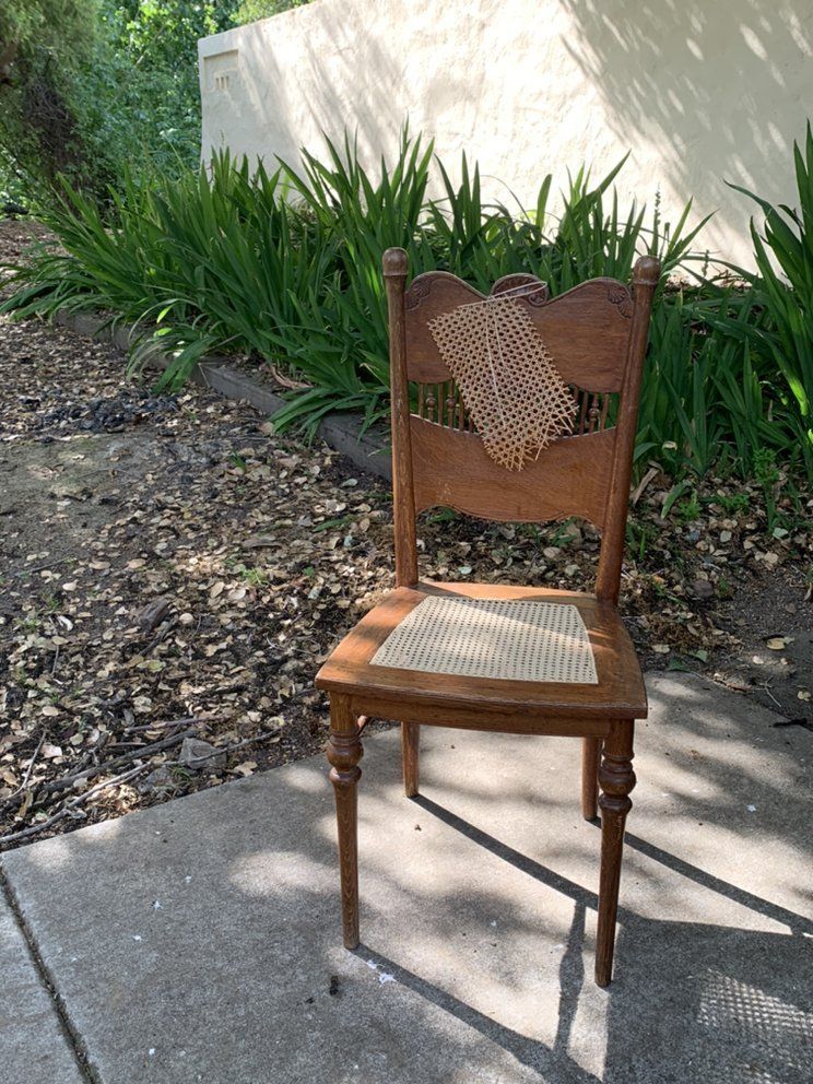 A wooden chair with a cane seat is sitting on a sidewalk.