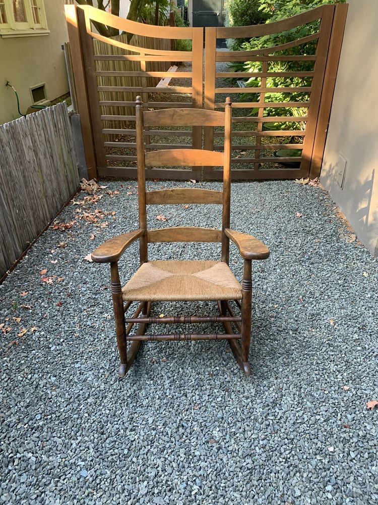A wooden rocking chair is sitting on gravel in front of a gate.
