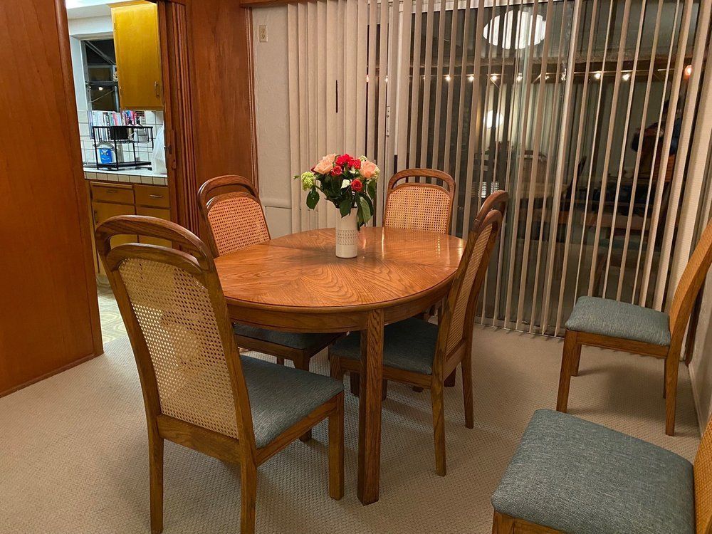 A dining room with a table and chairs and a vase of flowers on the table.