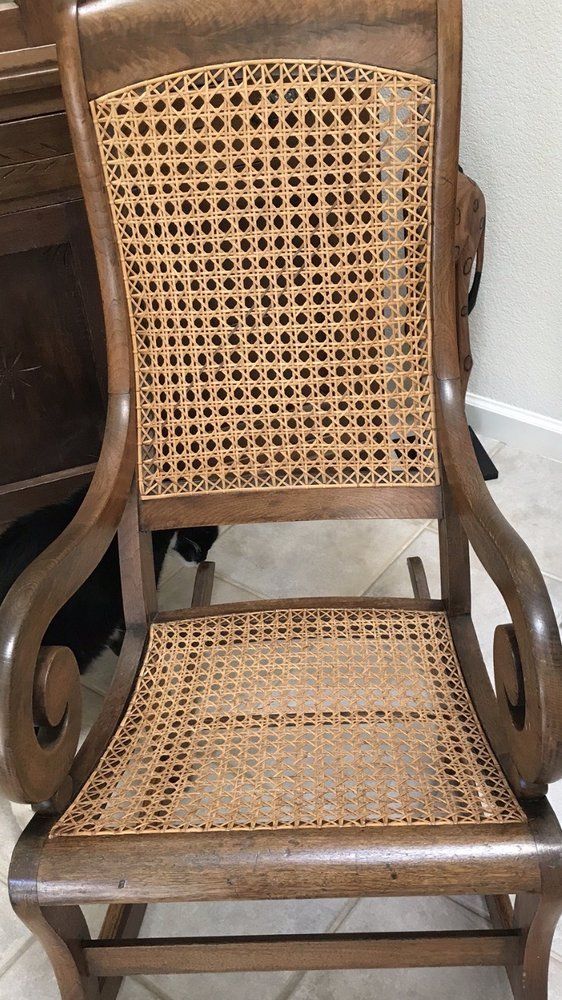A wooden rocking chair with a wicker seat is sitting on a tiled floor.