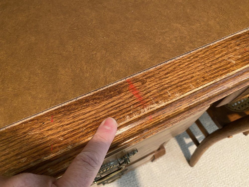 A person is pointing at a stain on a wooden table.