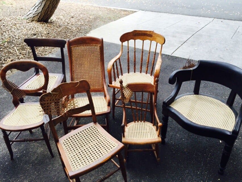 A group of chairs with wicker seats are sitting on the sidewalk